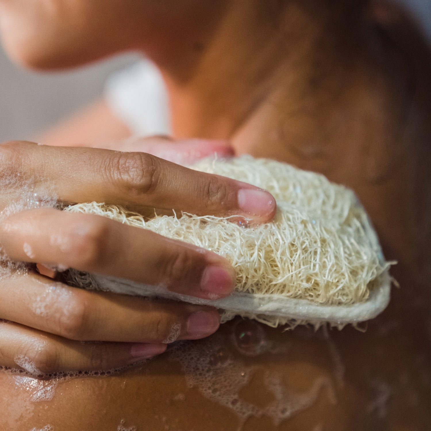woman washing her shoulder with a loofah sponge